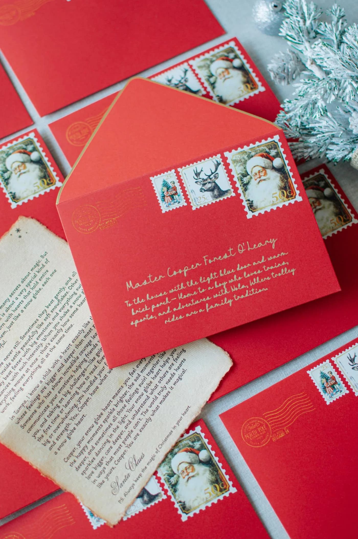 Personalised red envelopes with gold calligraphy arranged with a Santa letter and winter greenery