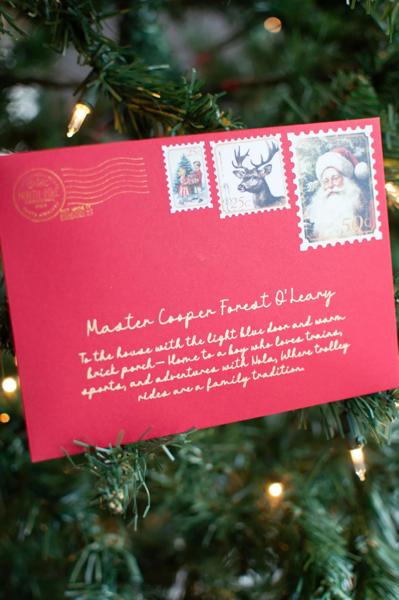 A personalised red Santa envelope with gold lettering resting among Christmas tree branches